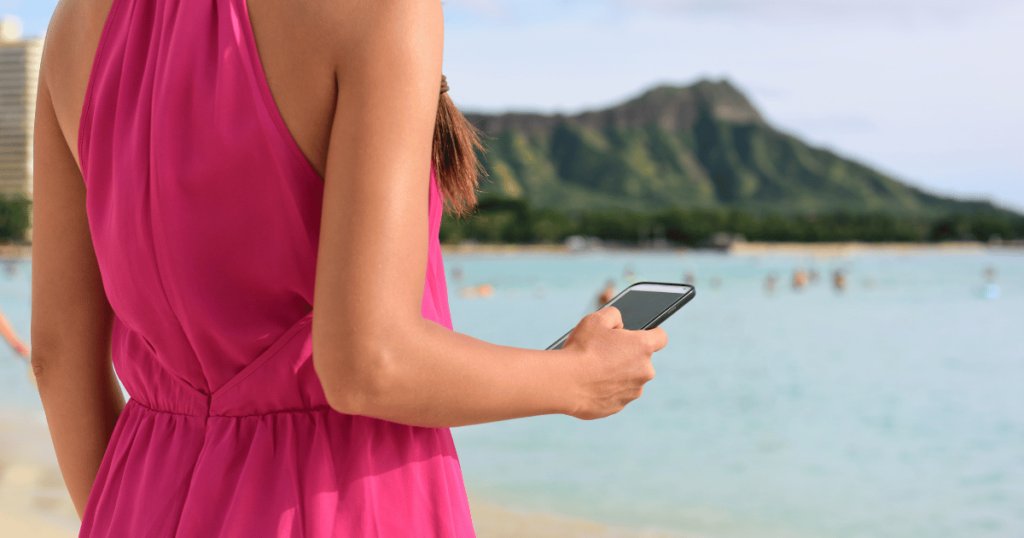 ホノルルの景色を背に、ピンク色のワンピースを着ている女性がUberアプリを使用している様子